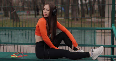 Sporty woman listening music in headphones outdoor sitting on benchの写真素材