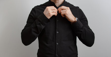 Unrecognizable man in black shirt fasten button at grey backgroundの写真素材