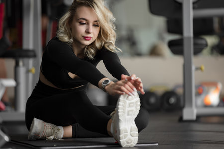 Woman stretching leg sitting on mat at the gymの写真素材