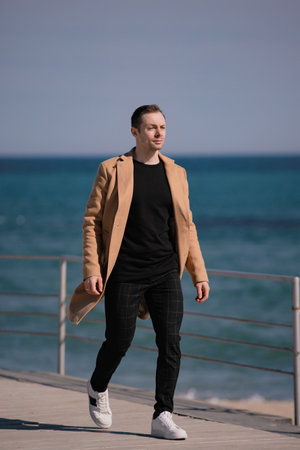 Stylish man in the beige coat walking along sea shoreの写真素材