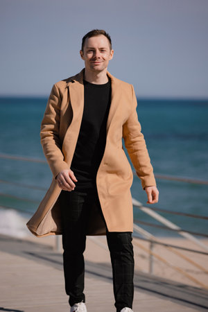 Stylish man in the beige coat walking along sea shoreの写真素材
