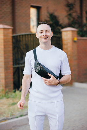 Stylish Caucasian man in white costume posing at the street holding a banana bagの写真素材