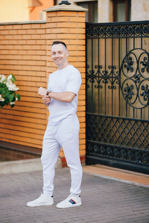 Handsome man in fashionable white costume posing at the street holding classical watchの写真素材