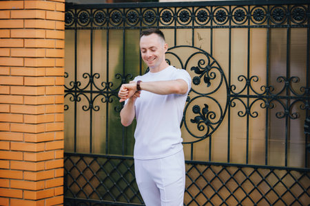 Handsome man in fashionable white costume looking time in classical watch at the streetの写真素材