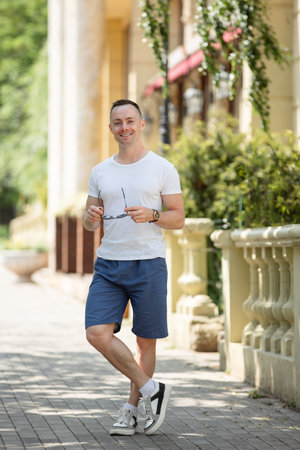 Handsome man in shorts and t-shirt posing with sunglasses in the city streetの写真素材