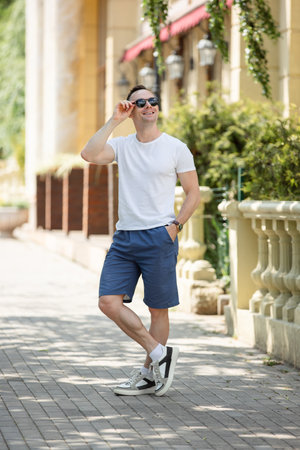 Handsome man in shorts and t-shirt posing with sunglasses in the city streetの写真素材