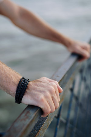 Male hands with black leather bracelet leaning on a fenceの写真素材