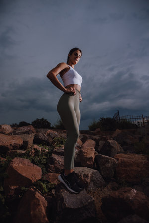 Portrait of sport woman standing on stones at the overcast cloudy day, dramatic viewの写真素材