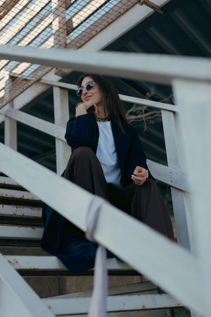 Stylish woman sitting on outdoor stairs at the spring day in sunglassesの写真素材