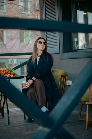 Happy woman sitting at outdoor cafe with bouquet of tulips on a tableの写真素材