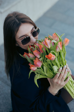 Happy woman sniff tulip flowers in city street at spring dayの写真素材