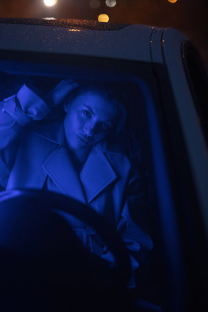 Lady posing in the car in blue light at nightの写真素材