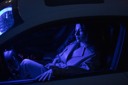 Lady posing in the car in blue light at nightの写真素材