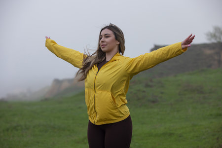 Happy woman with raised hands enjoy the nature and overcast weather in yellow jacketの写真素材