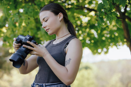 Woman photographer looking photos in a camera under treeの写真素材