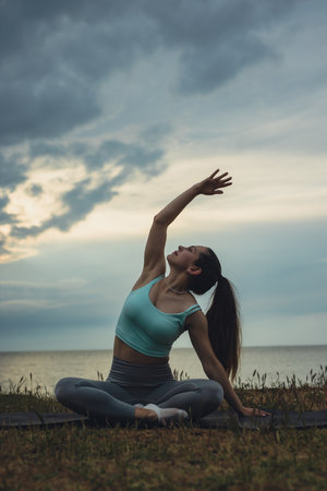 Woman doing yoga stretching exercises on a hill against sea backgroundの写真素材