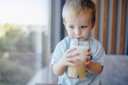 A little boy drinking lemonade with straw in a cafeの写真素材
