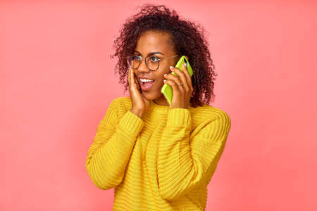 Emotional cheerful African female talks on mobile phone, shares impressions with interlocutor,...
