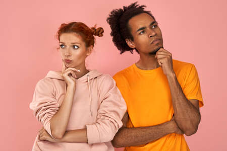 Thoughtful ginger woman and dark skinned man do not look at each other, being in deep thoughts,...
