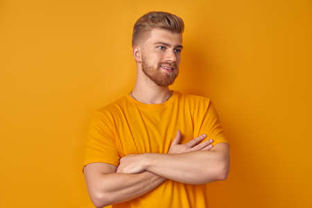 Cheerful man holding his arms crossed and laughing looking away on a background of a yellow wall....