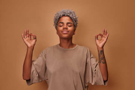 African woman meditates indoor keeps hands in mudra gesture has eyes closedの写真素材