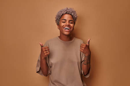 Portrait of beautiful young African woman smiling with thumbs up hand gestureの写真素材