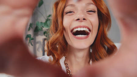 Happy redhead woman making shape heart gesture with hands on eve of Valentineの写真素材