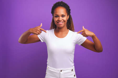 Young African American woman smiles and points fingers at snow-white blouse