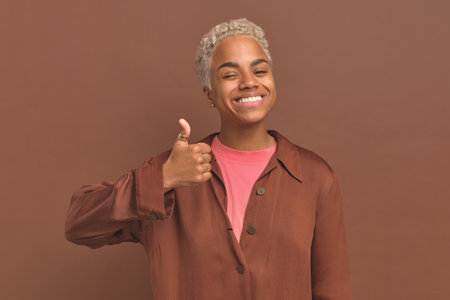 Young positive African American woman thumbs up and smiles stands in studioの写真素材