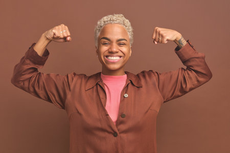 Young happy African American woman showing off biceps stands on brown backgroundの写真素材