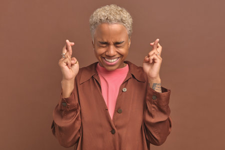 Young African American woman crosses fingers and closes eyes waiting for lotteryの写真素材