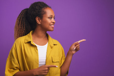 Young beautiful African American woman points to side with two fingersの写真素材