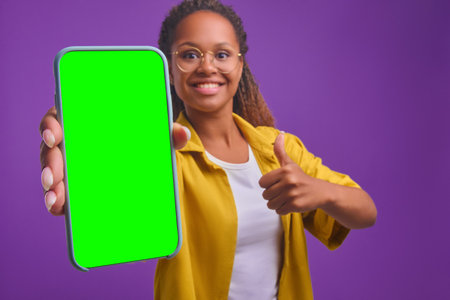 Young smiling African American woman holds out phone to camera shows thumbs upの写真素材