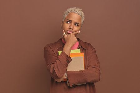 Young pensive curly African American woman student with textbook and workbooks