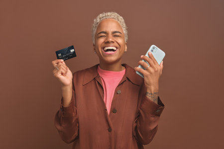 Young African American woman with credit card and phone enjoy online shoppingの写真素材