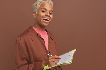 Young African American woman with notebook and pen in hands stands in studioの写真素材