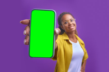 Young positive African American woman holds out green screen phone to cameraの写真素材