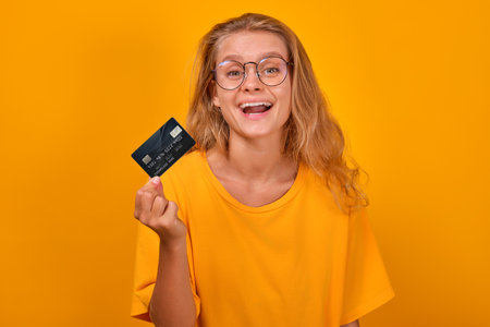 Young cheerful pretty Caucasian woman showing credit card and laughing