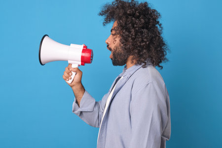 Young screaming Arabian man marketer with megaphone in hands stands in studioの写真素材