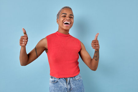 Young laughing excited African American woman shows thumbs up stands in studio