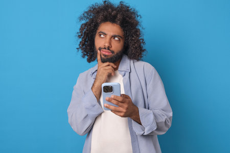 Young thoughtful Arabian man millennial uses mobile phone stands in studio