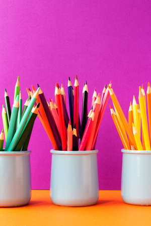 Three ceramic glasses with colored pencils on trend saturated pink and orange background.Back to school concept. Education background.の写真素材