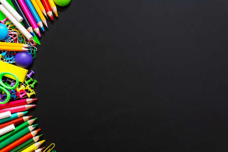 Top view on blackboard with school supplies. Multi colored vibrant pencils, paints, paper clips and other objects. Copy space.の写真素材