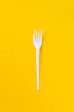 One white plasti fork on saturated yellow background as a symbol of consumption. Eco and fast food concept.の写真素材