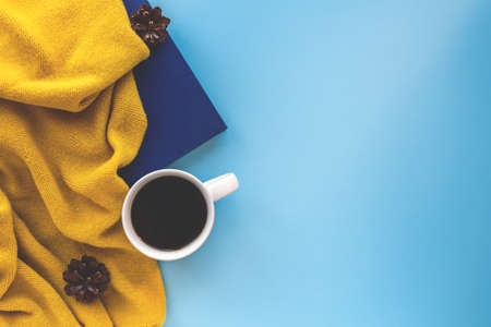 Hot cup of coffee, book or daily planner and warm scarf in autumn colors on contrast blue background. Flatlay of still life concept. Copy space.の写真素材