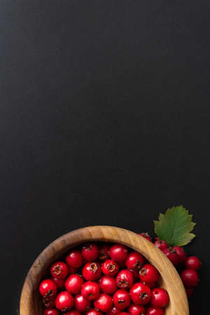 Top view of red berries in wooden bowl on black background. Autumn concept. Copy space.