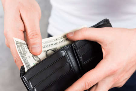 unrecognizable young man holding black leather wallet with two dollars in hands. Close up photo....