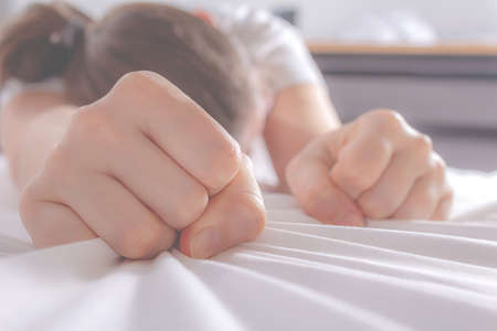 Unrecognizable depressed woman after domestic violence. Woman's fists clenched in fear, crumpled sheet.の写真素材