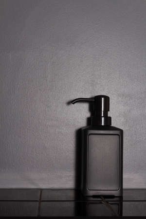 Minimal black in bathroom interior. Copy space. Conceptual trendy soap dispenser on glossy tile and matte wall. Totally black interior.の写真素材