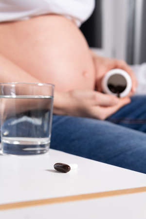 Unrecognizable Pregnant Woman in bed holding antipyretic and pain medication pills in hand before...